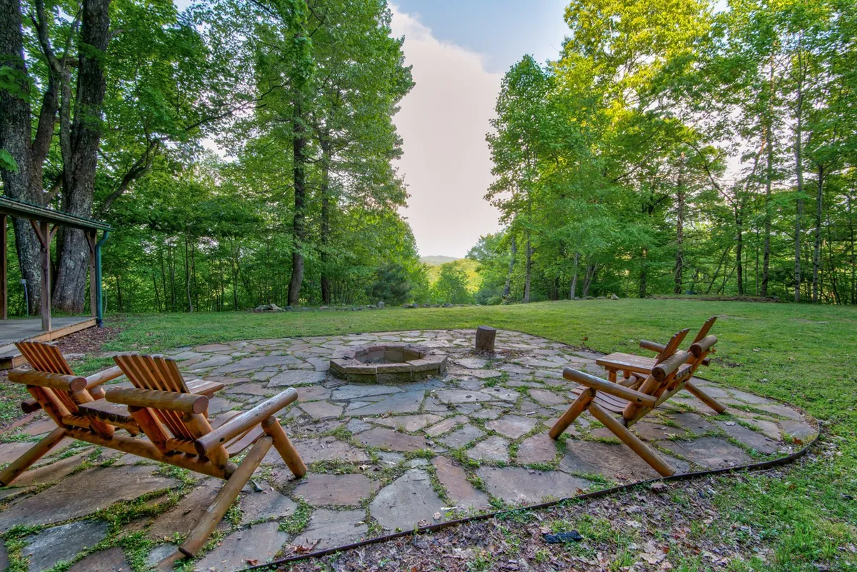A cozy firepit area surrounded by wooden chairs and nestled among tall trees. The inviting setup suggests gathering for stories, s'mores, or stargazing, with a strong sense of nature and togetherness.