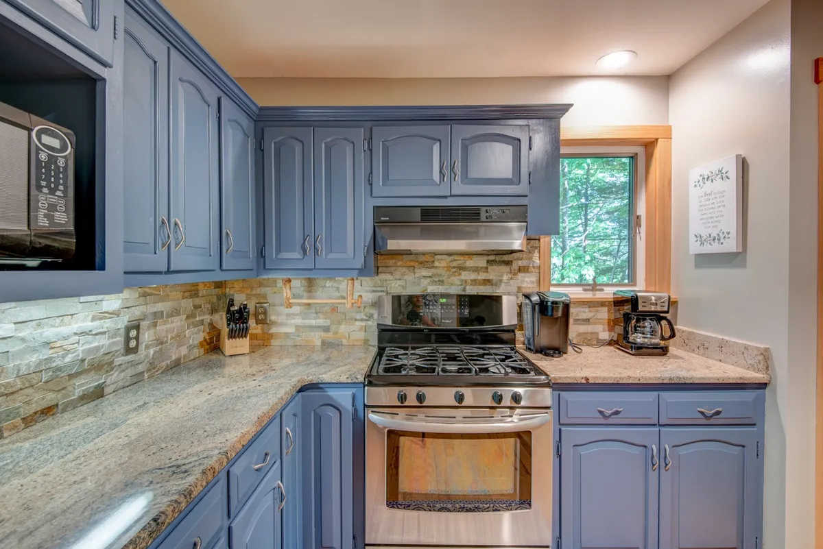 This image provides a clear perspective of the modern kitchen, highlighting blue cabinetry, granite countertops, stainless steel appliances, and a window view. It communicates both style and functionality, capturing the kitchen as a gathering point for meal prep and socializing.