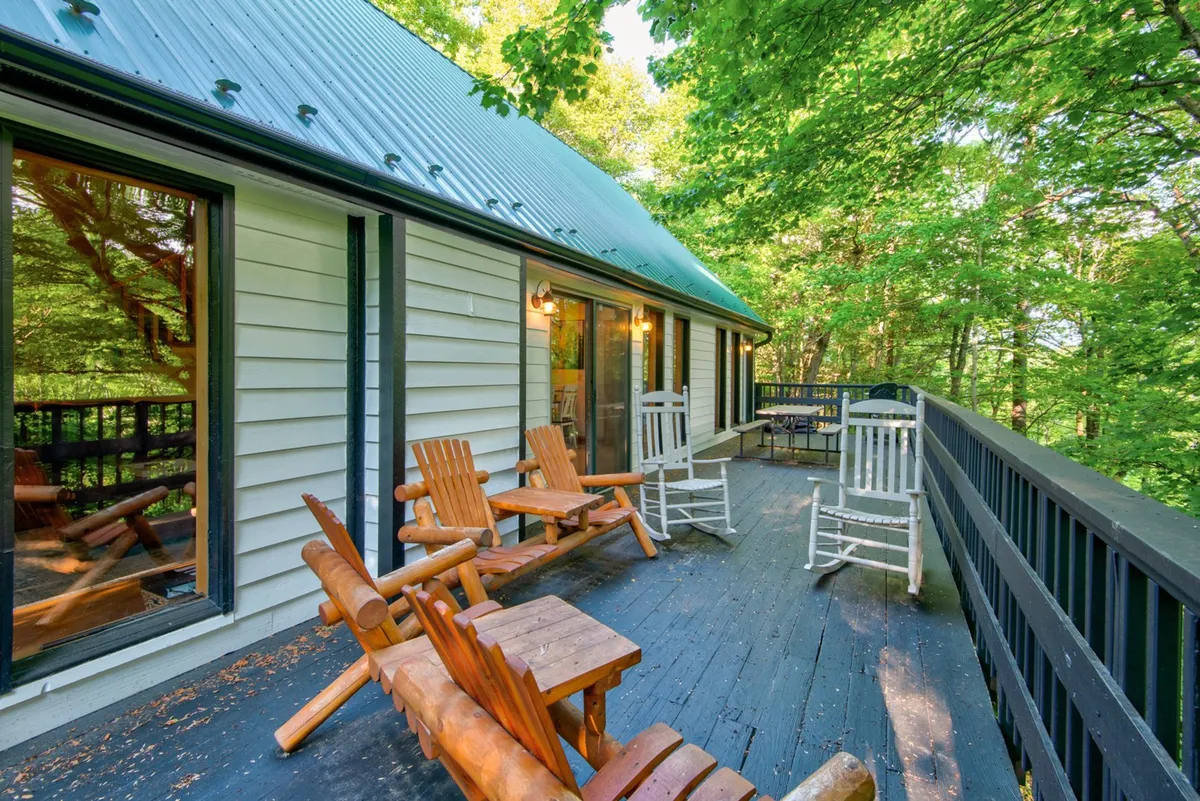 This image showcases a peaceful deck area with wooden rocking and Adirondack chairs overlooking lush greenery. The inviting seating hints at a dog-friendly environment where guests can relax outdoors, enjoy mountain air, and perhaps rest after a long walk with their pets.