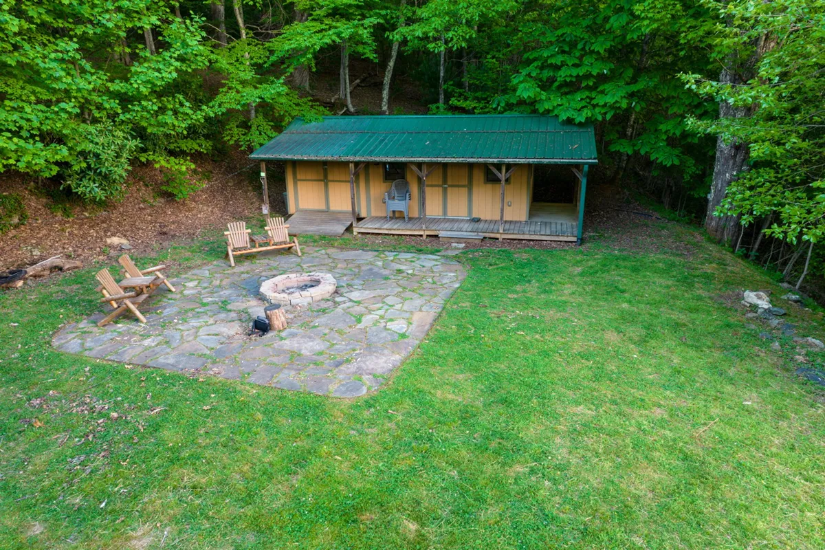 This image displays a welcoming outdoor fire pit area with Adirondack chairs arranged around a glowing fire, set beside a cozy cabin and surrounded by nature.