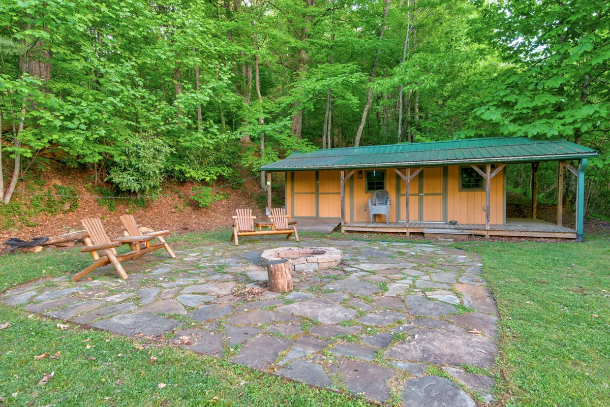 A charming yellow cabin sits amid lush greenery with a stone fire pit and Adirondack chairs out front. The scene suggests both relaxation and adventure, inviting guests to enjoy nature, campfire gatherings, and seasonal activities right at the doorstep.