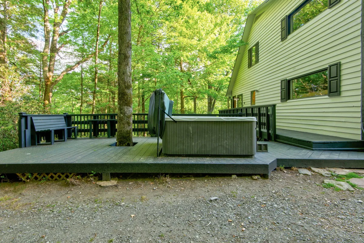 An exterior shot featuring a private hot tub on a wooden deck, surrounded by trees and a bench, exuding tranquility and a close connection to nature.