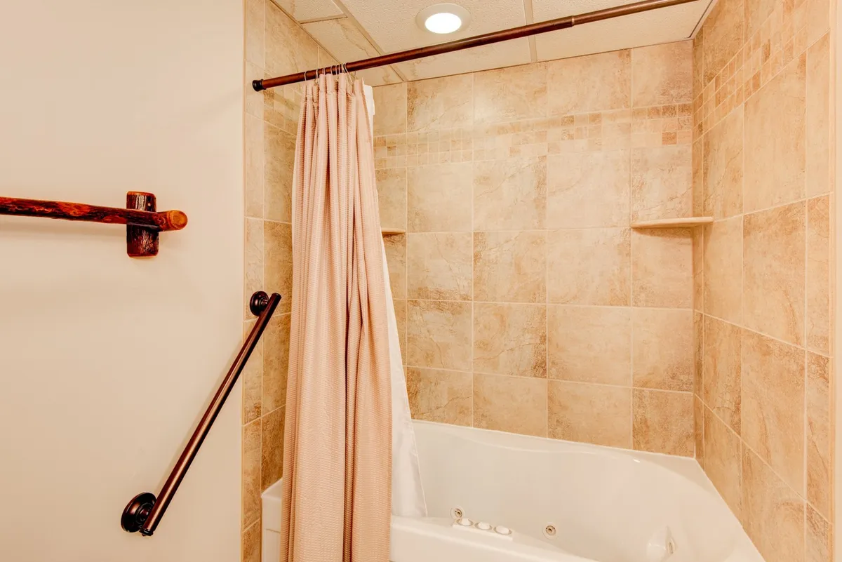 A soothing bathroom scene showcasing a jacuzzi tub surrounded by natural stone tiles, paired with a shower curtain. The tranquil ambiance is perfect for relaxation and self-care routines.