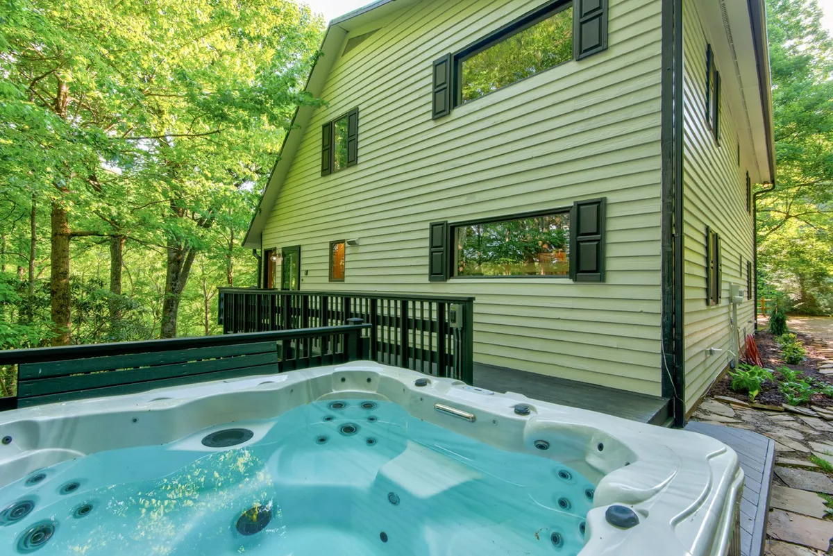 An exterior shot highlighting a bubbling hot tub on a spacious deck with the house in the background and lush greenery all around. The scene exudes tranquility and the promise of relaxing evenings under the stars—perfect for unwinding after mountain adventures and fostering group connection.