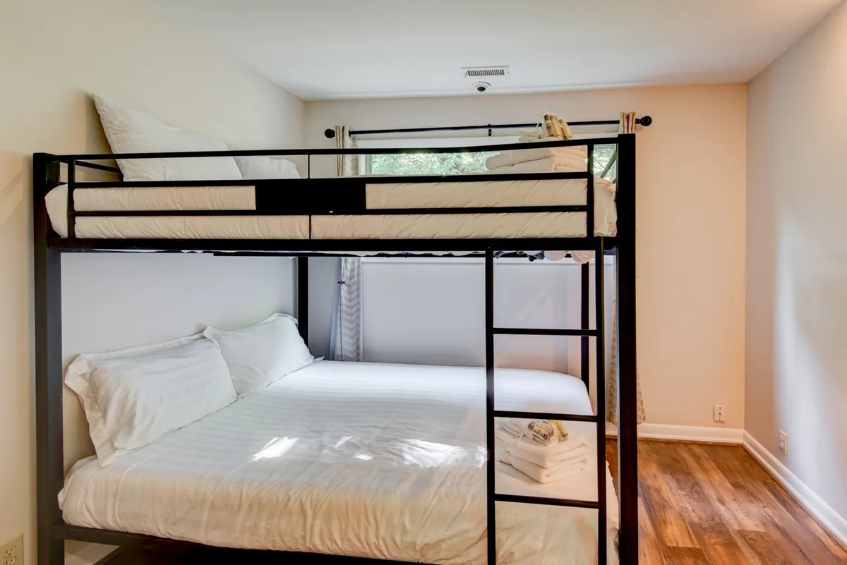 A bright bunk room featuring a bunk bed with soft bedding, enhanced by ample natural light streaming in from a window. The playful and cozy setup is ideal for kids or friends, evoking feelings of fun and togetherness.